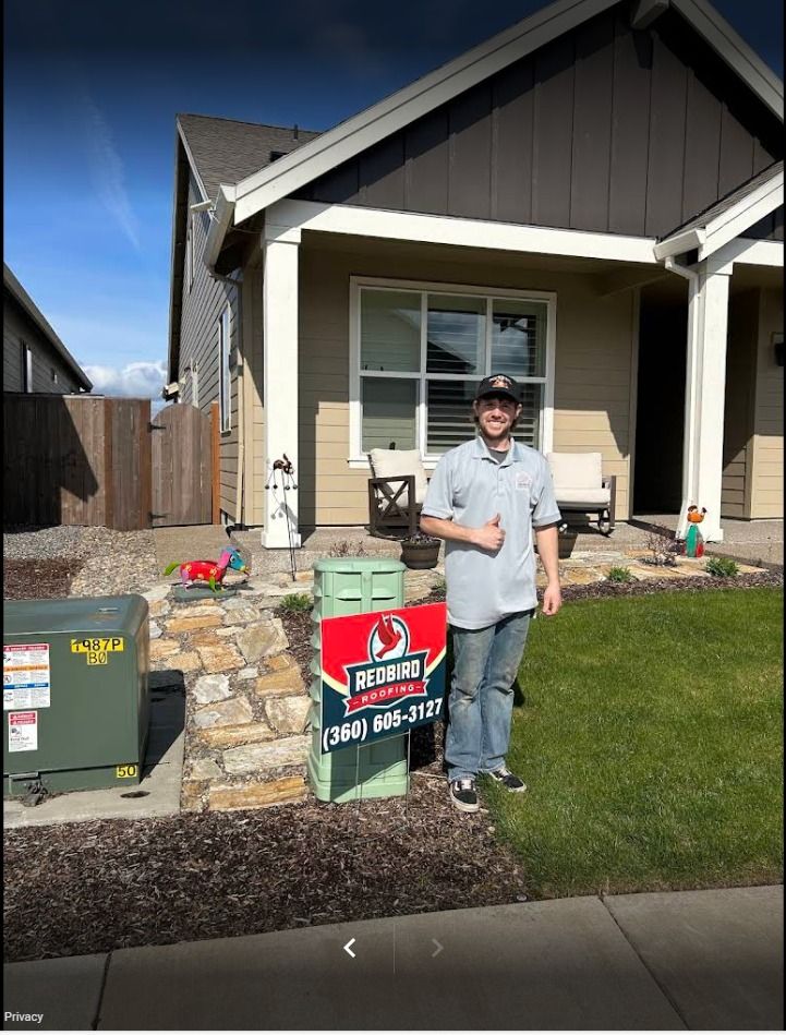 A person in a light blue shirt gives a thumbs up next to a Redbird Heating and Cooling sign in front of a tan house.