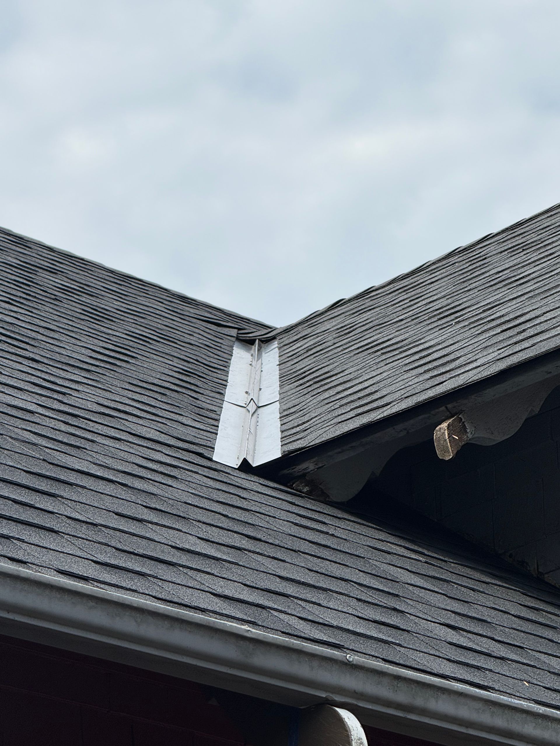 A close-up of a roof valley with metal flashing installed between two shingled roof sections.
