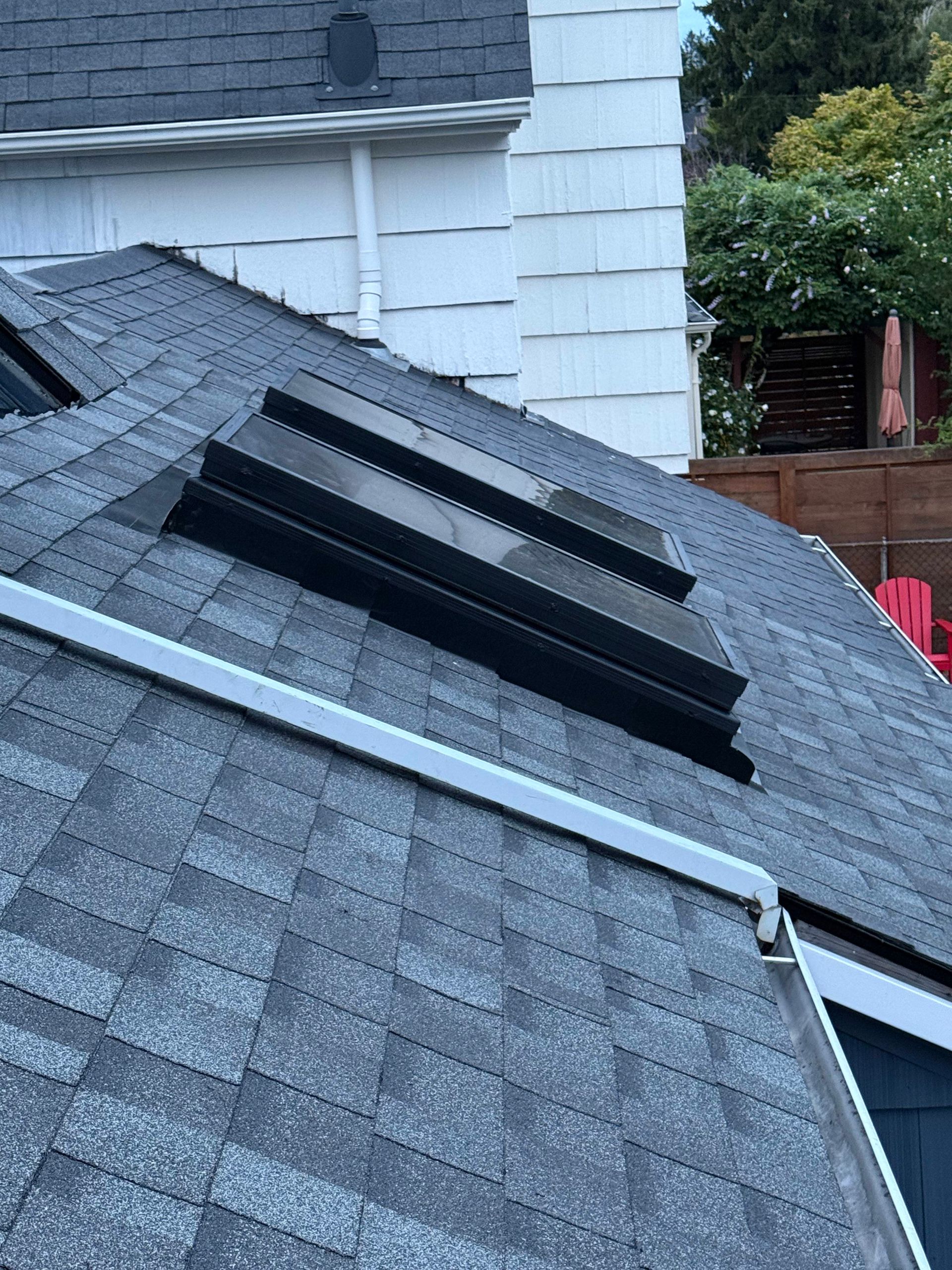 A slanted shingled roof features two rectangular skylights, with a white wall and a white trim edge visible in the back.