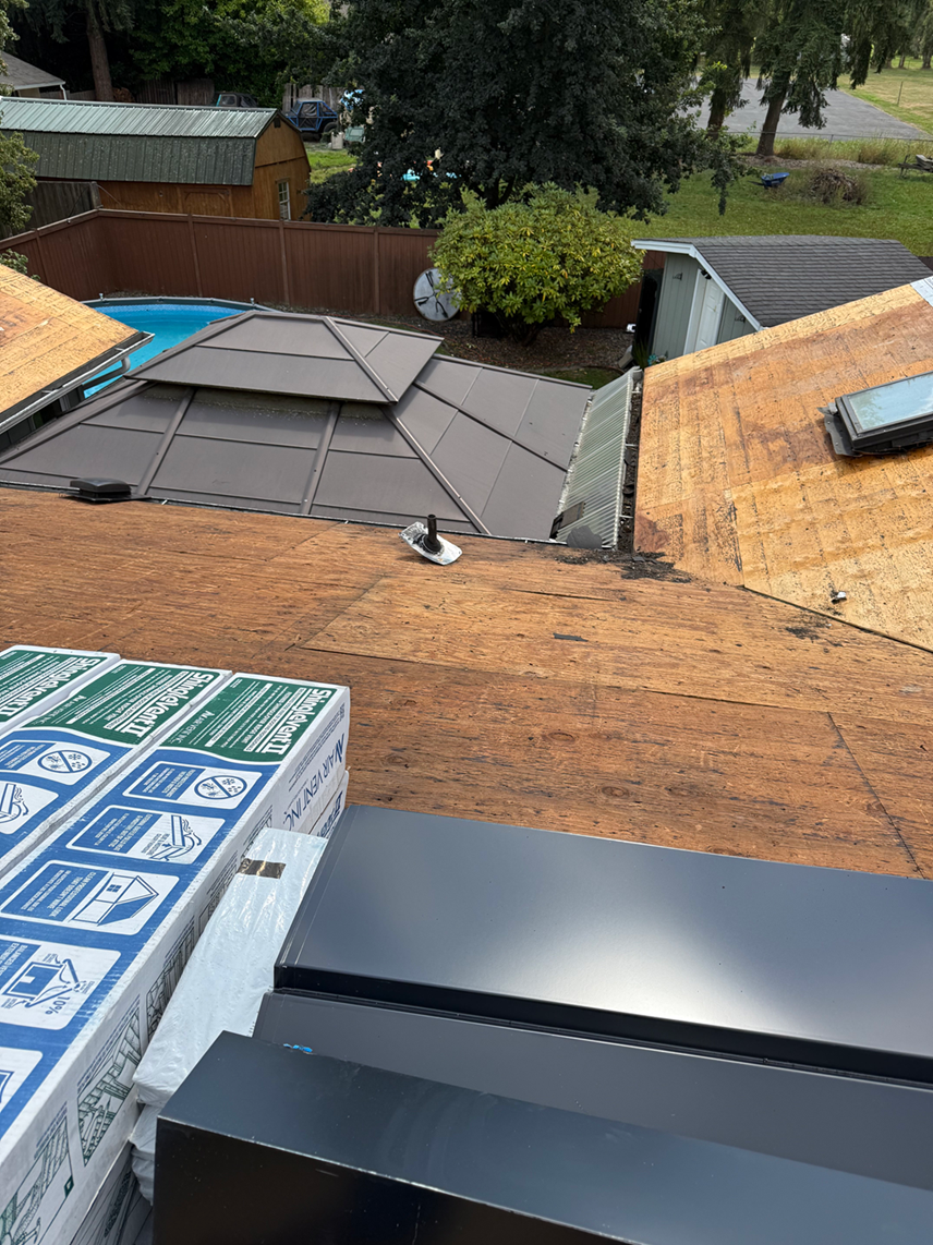 A view from a roof under construction, showing bare wooden decking, roofing materials, a gazebo, and a swimming pool below.