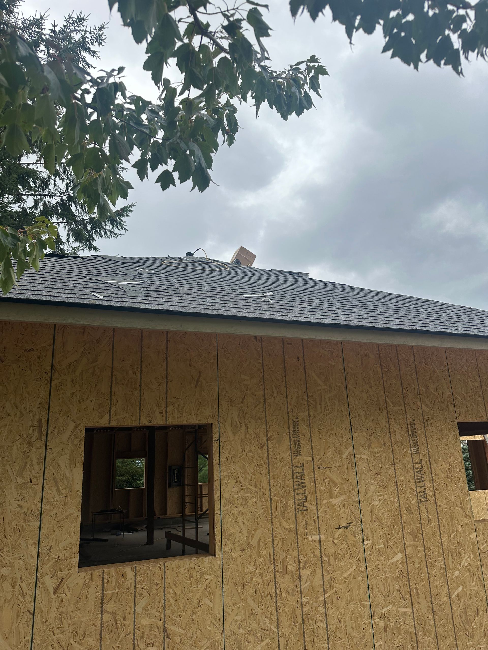 An exterior view of a building under construction, featuring oriented strand board (OSB) walls and a shingled roof.