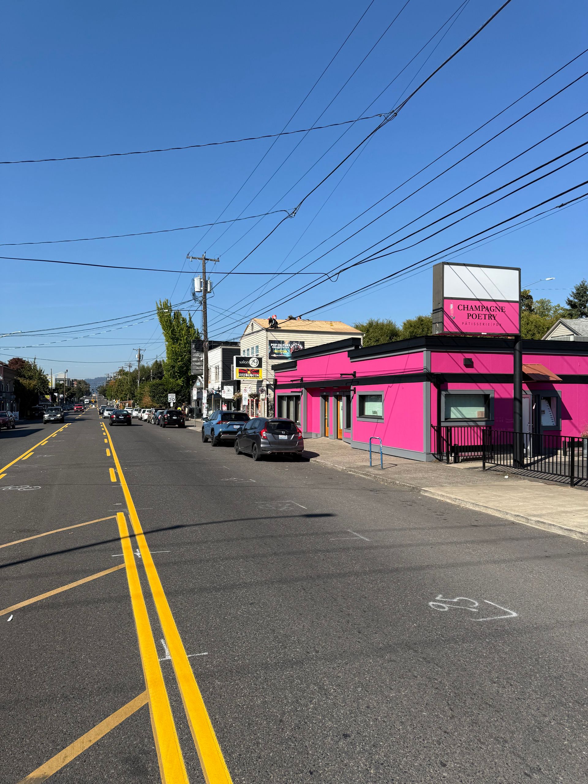 A bright pink building with a prominent sign sits on a sunny street corner next to parked cars and utility lines.