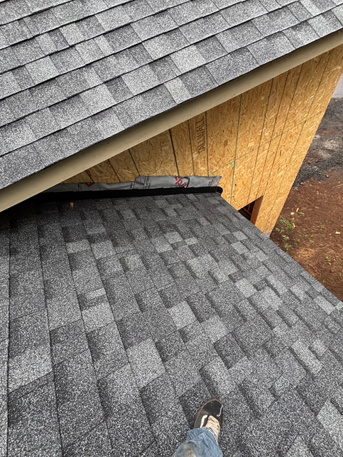 A close-up of a roof showing a transition between two shingled roof sections, with exposed plywood siding above.