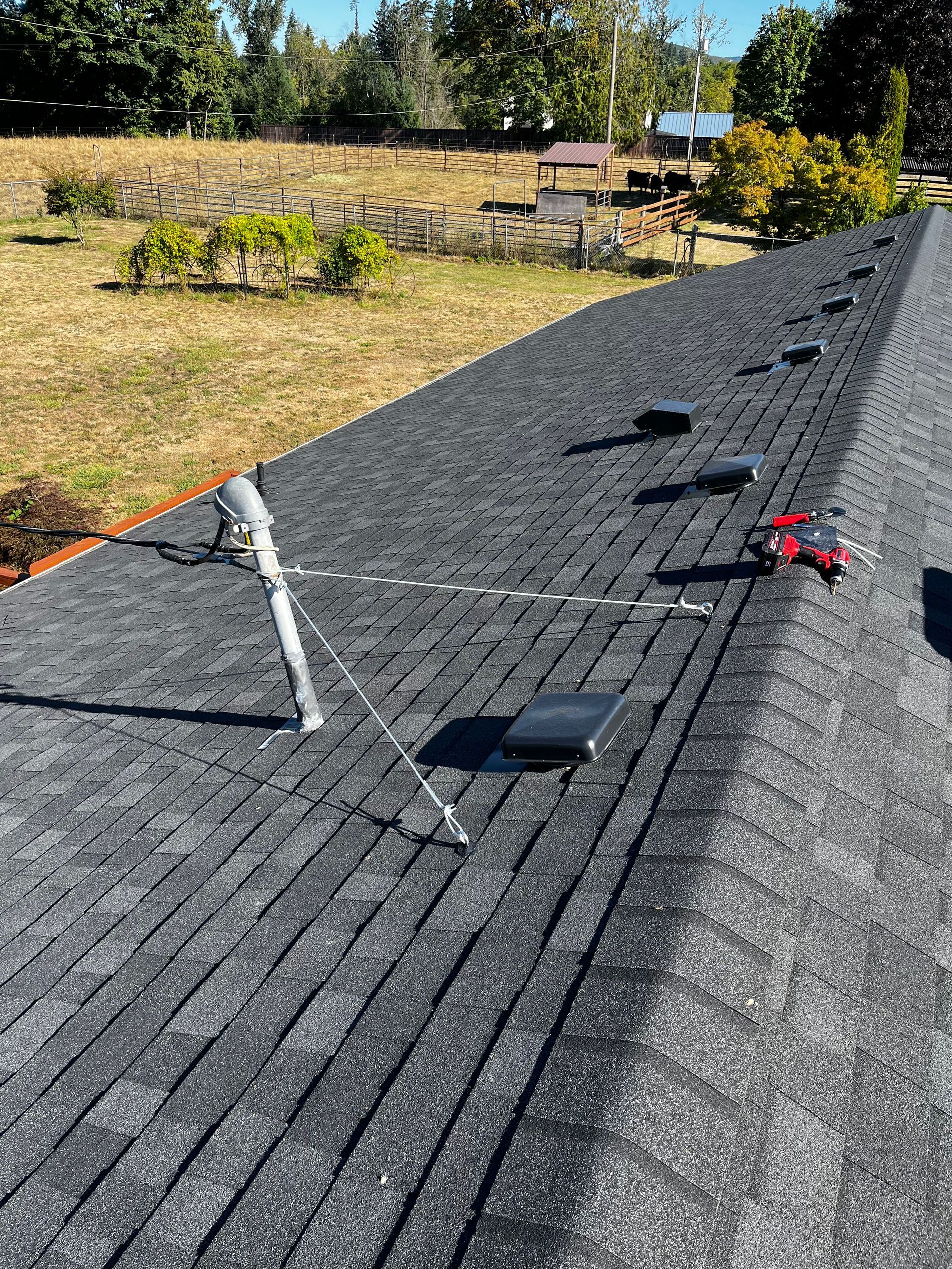 A gray asphalt shingled roof with a metal utility mast, ventilation vents, and a red object near the peak.
