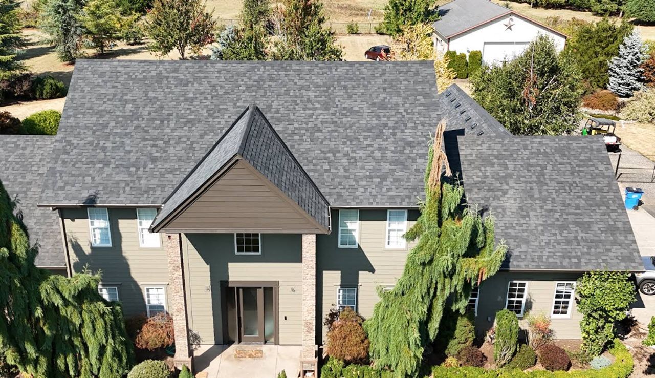 An aerial view of a two-story home with a gray shingled roof, olive-green siding, and a prominent front entryway.