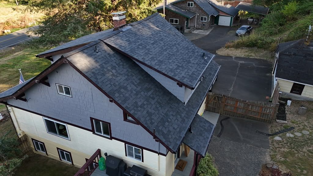 Aerial view of a house with a dark gray roof and white exterior in a wooded yard