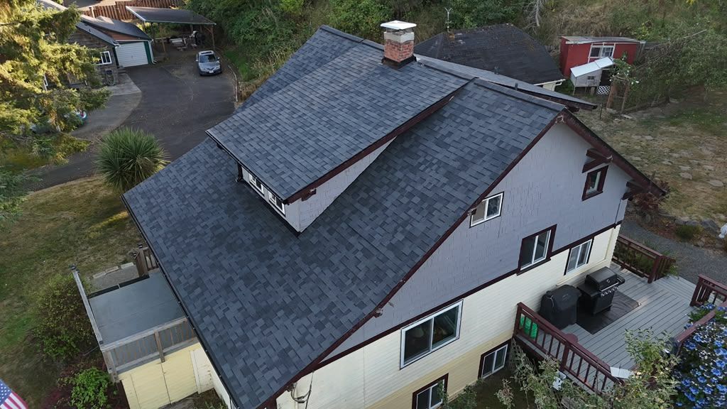 Overhead view of the finished dark shingle roof and chimney with clean ridge lines