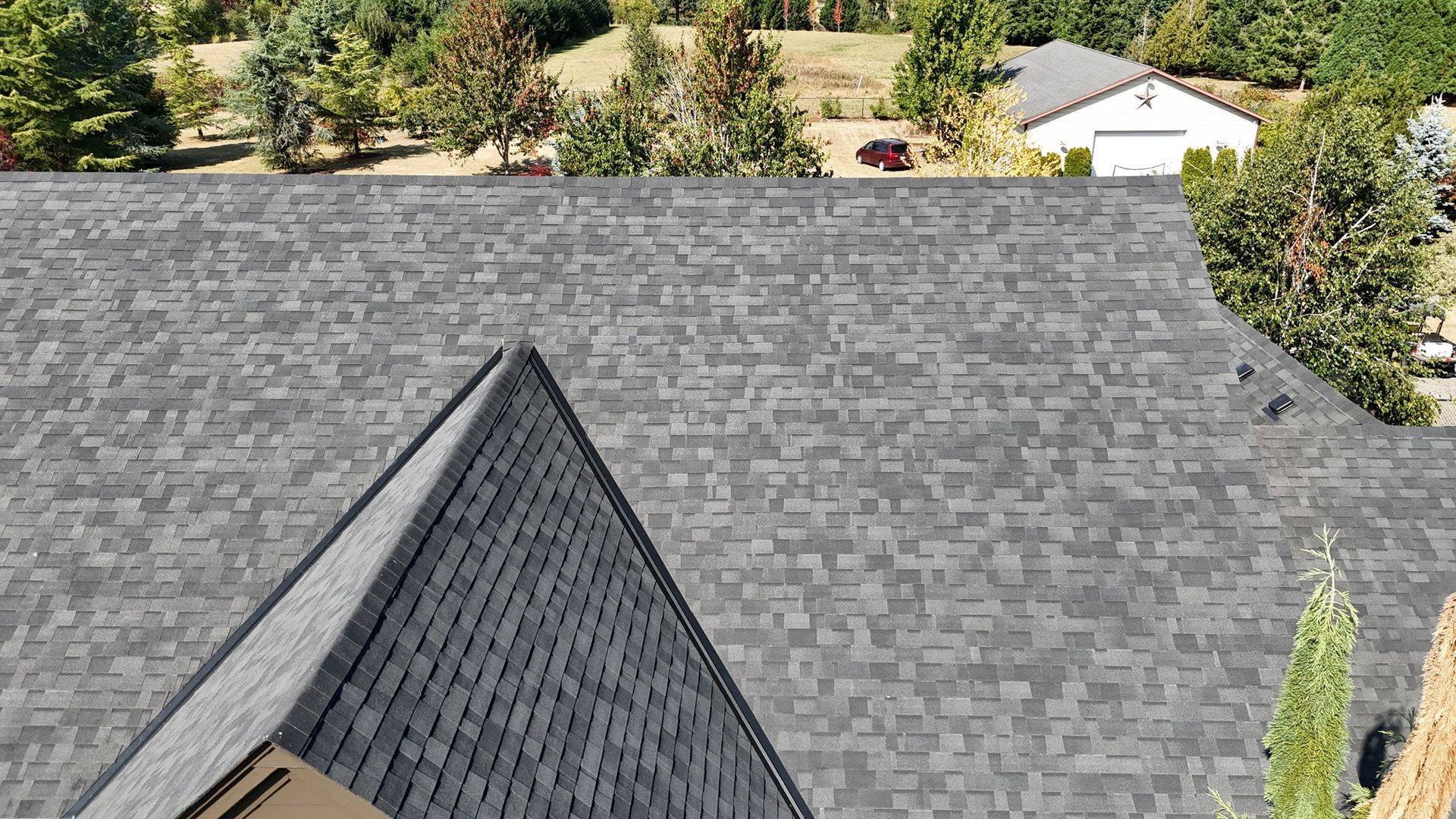 A high-angle view of a grey architectural asphalt shingle roof with a prominent triangular gable on a sunny day.
