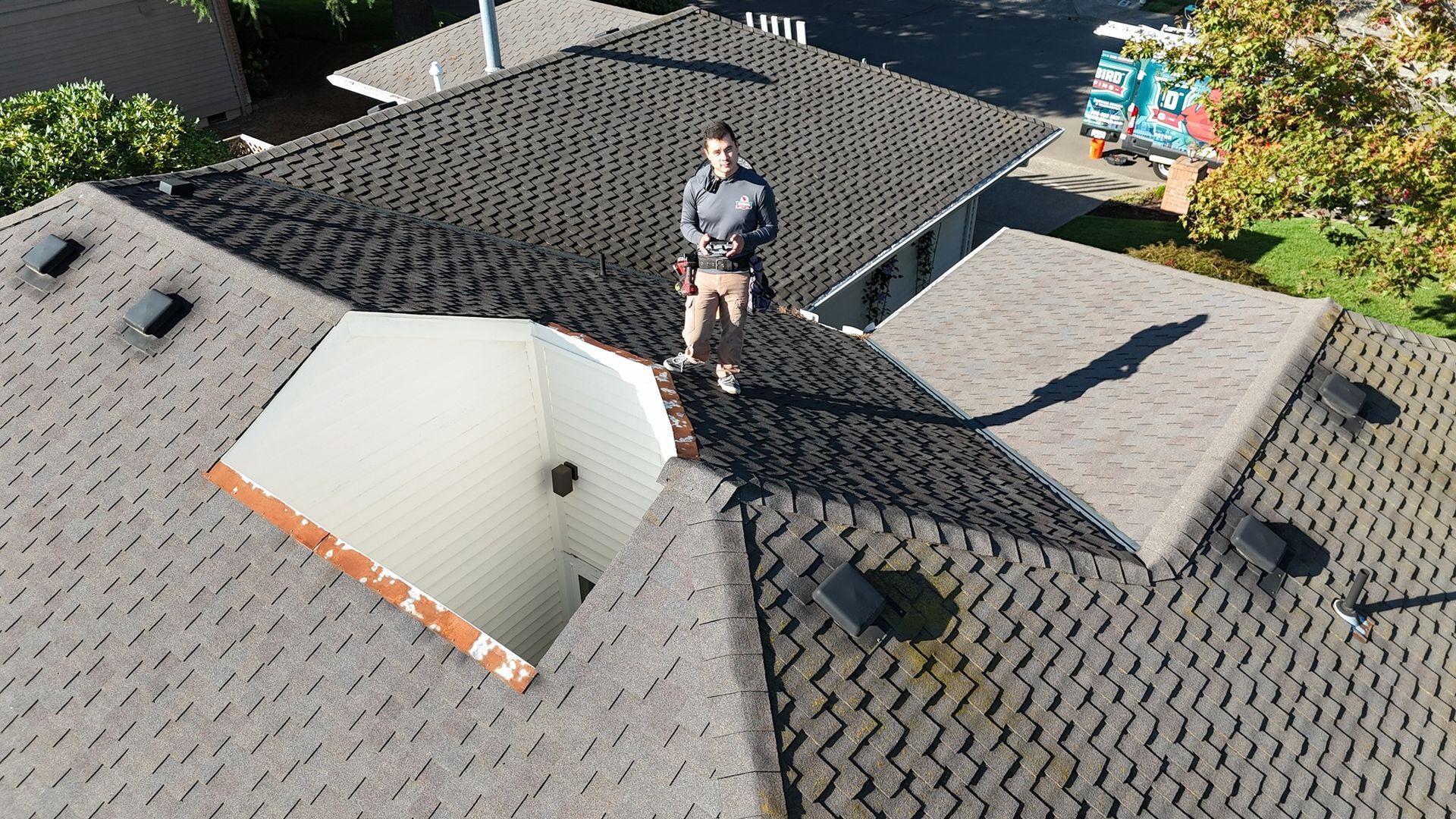 A worker stands on a dark shingled roof next to a white recessed interior courtyard.
