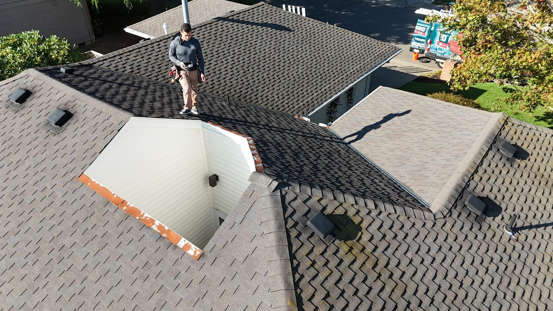An aerial view of a person standing on a shingled roof next to a large, open-air light well or atrium.