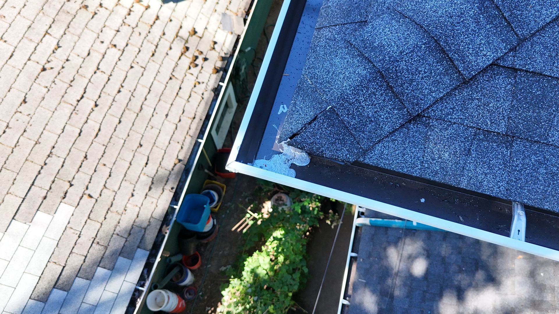 A top-down view of a home exterior showing shingles, a flat roof section with pooling water, and a backyard area below.