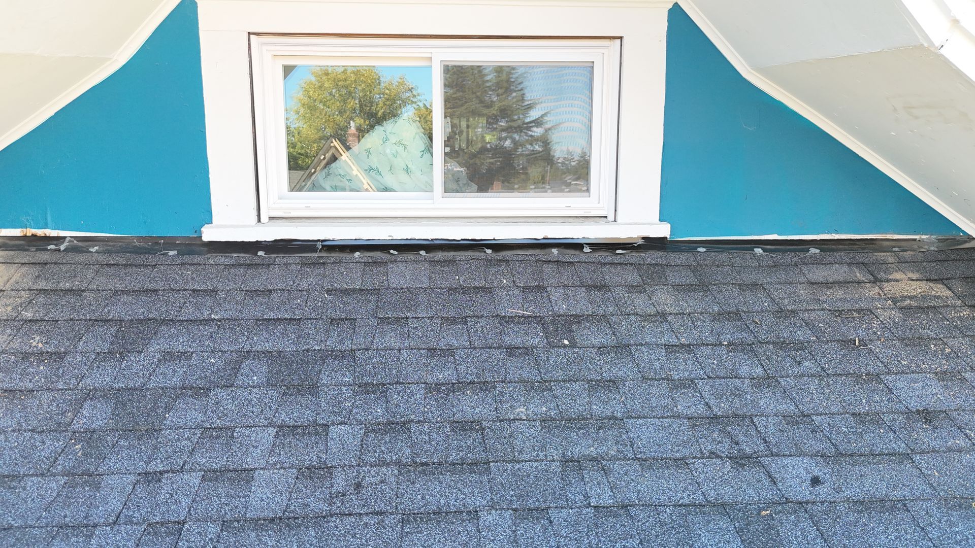 A horizontal sliding window centered on a dark shingled roof, flanked by teal-painted triangular dormer walls.
