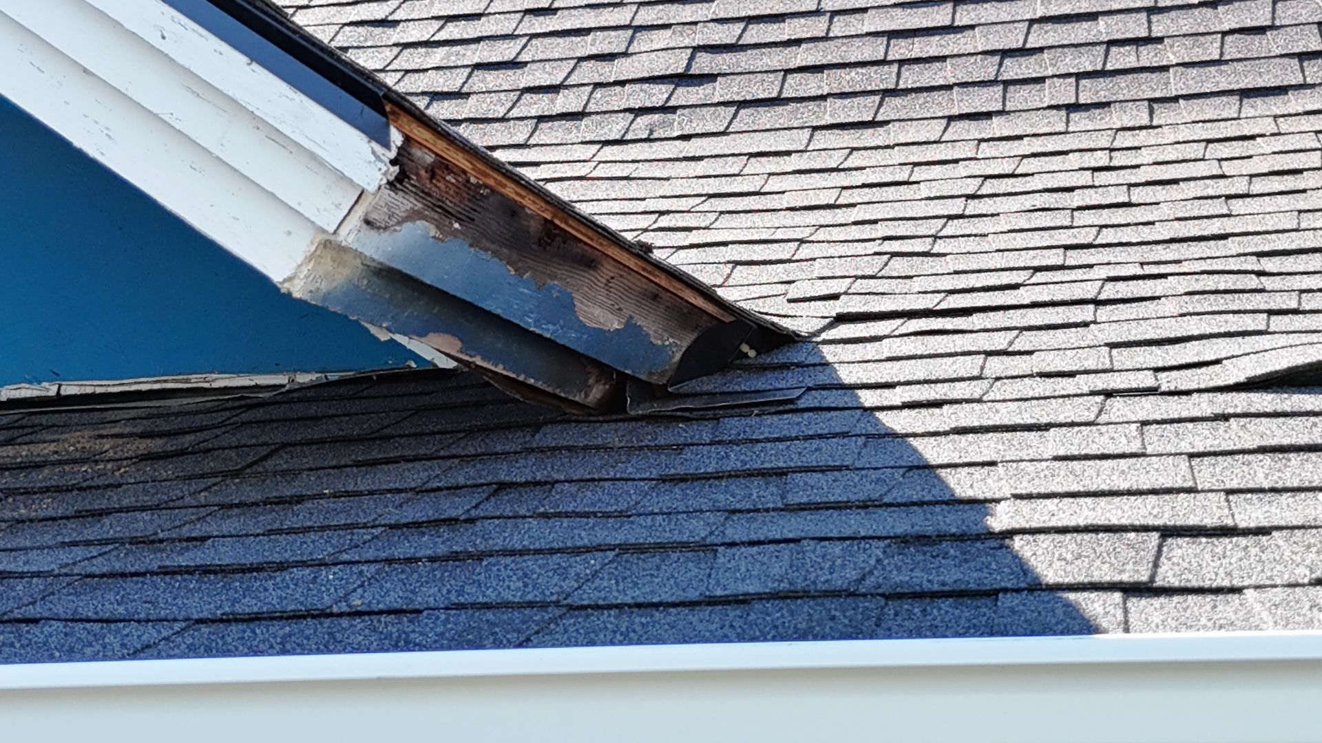 Damaged roof fascia and shingles showing wood rot and peeling paint at the gable edge.