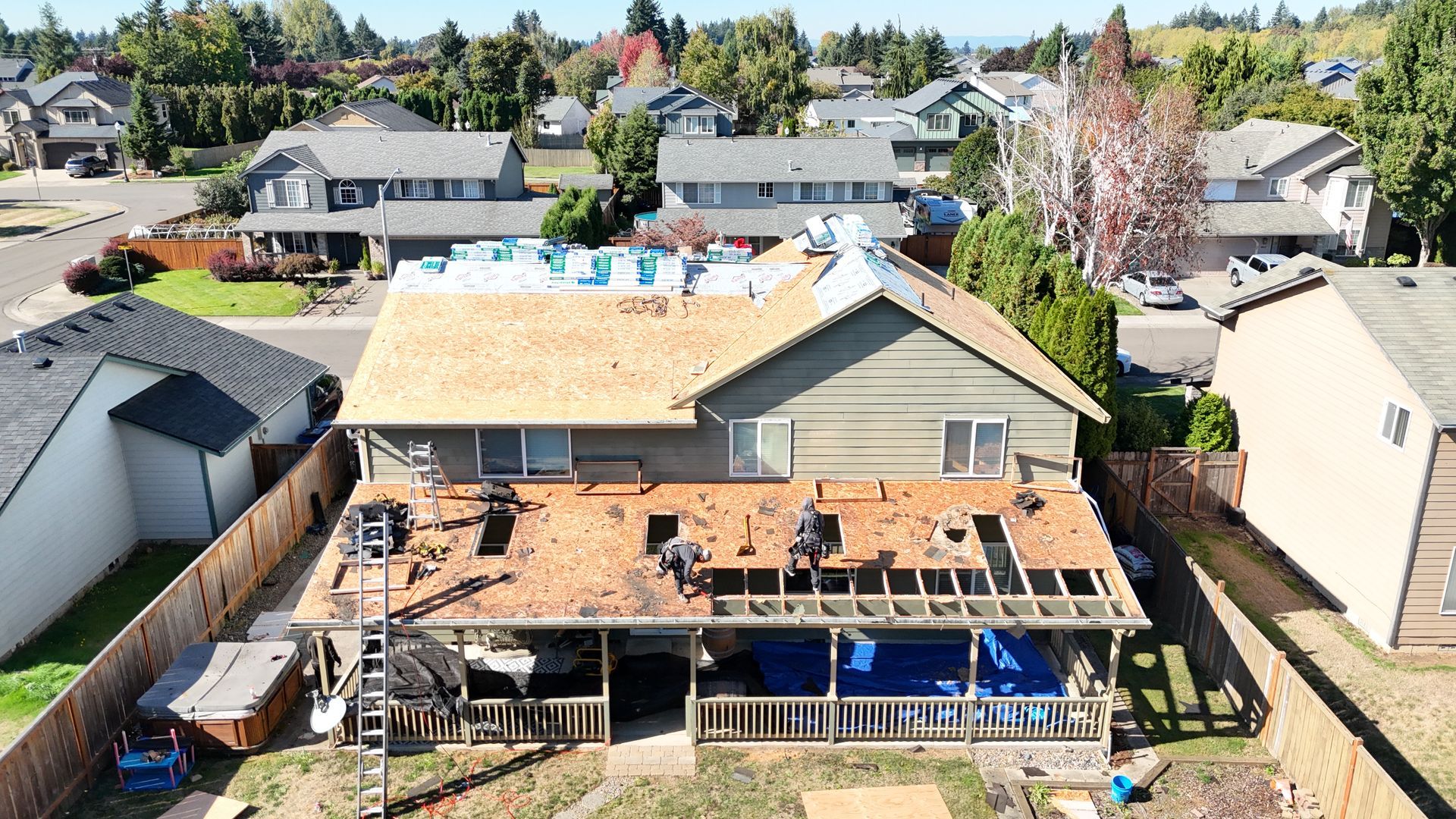 An aerial view shows contractors working on the wooden roof deck of a two-story suburban house during a renovation.