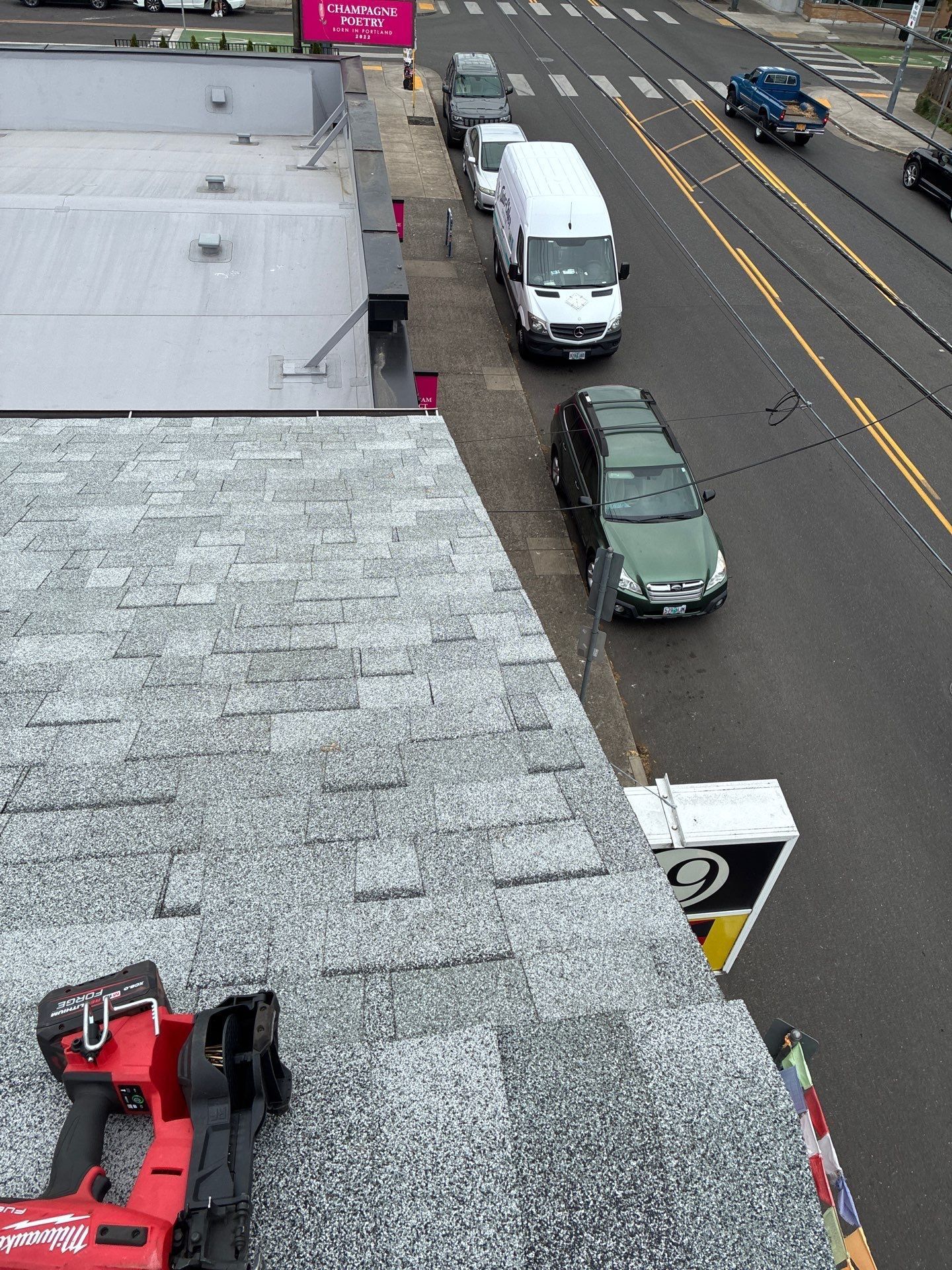 Overhead view of a street with parked vans beside a building and a red car in the lower left.