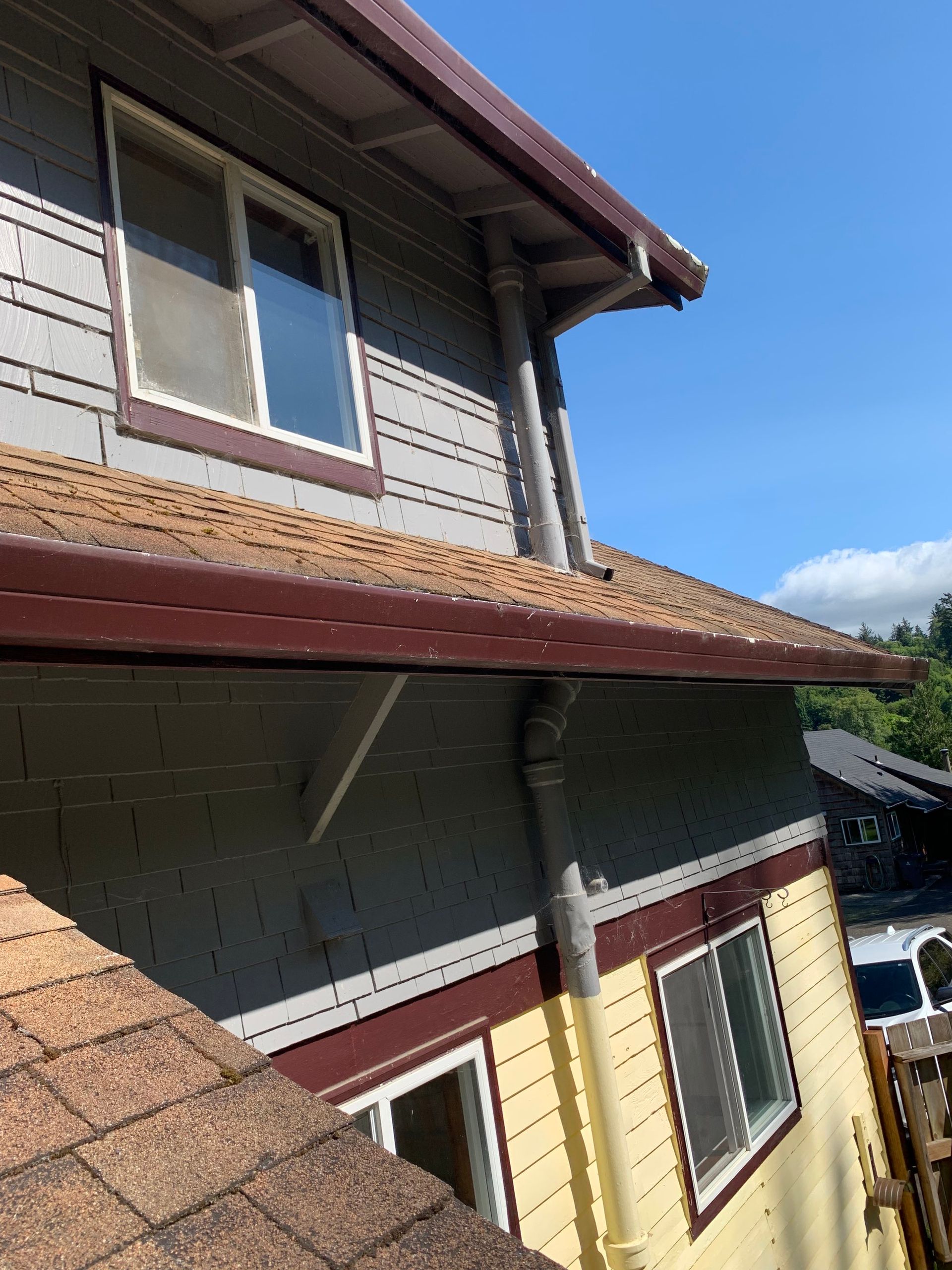 Aging roof edge and downspout at a low-slope section of the home before new roofing and gutters