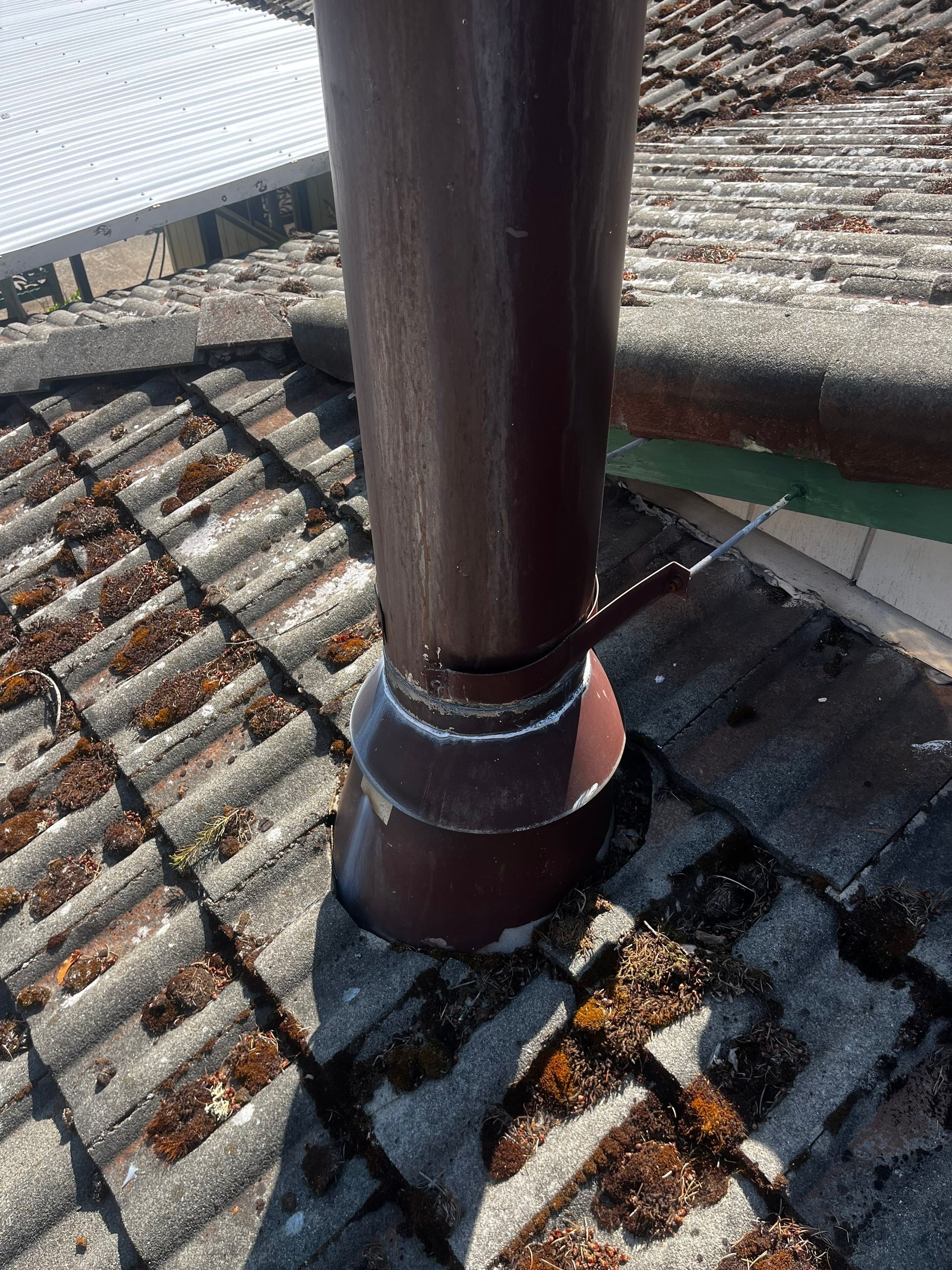 Close-up of cracked, moss-filled concrete roof tiles around a pipe with new flashing