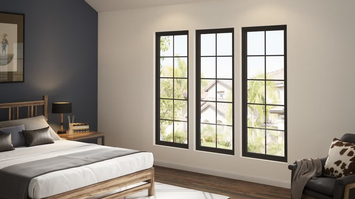 A modern bedroom with a wooden bed, a dark accent wall, and three tall windows with black frames looking onto trees.