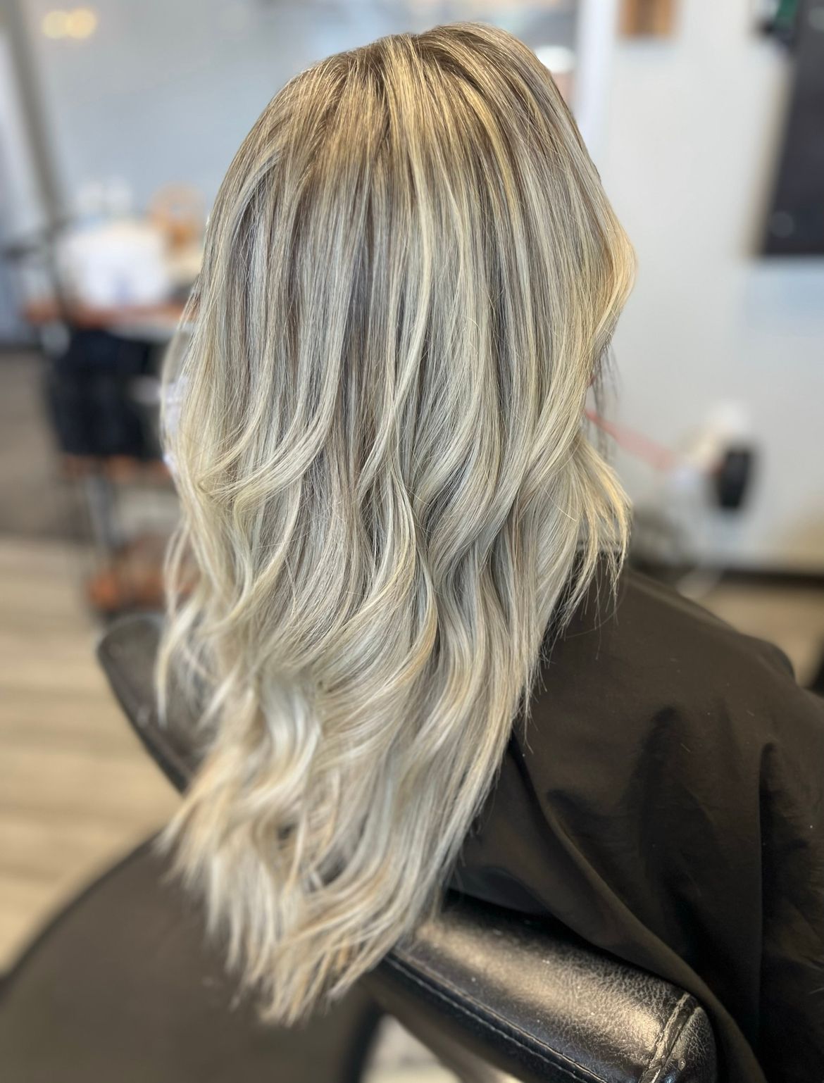 A woman with long blonde hair is sitting in a chair in a salon.