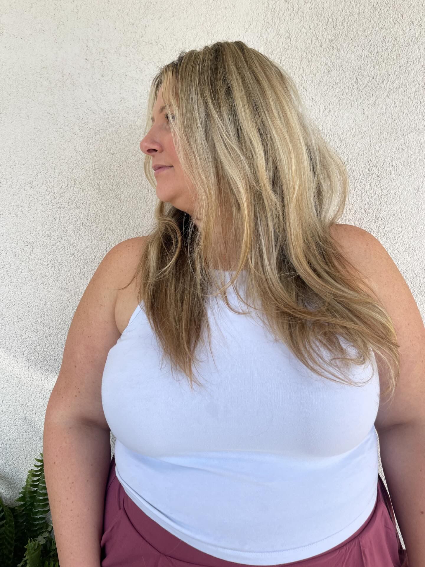 A woman in a white tank top and burgundy skirt is standing in front of a wall.