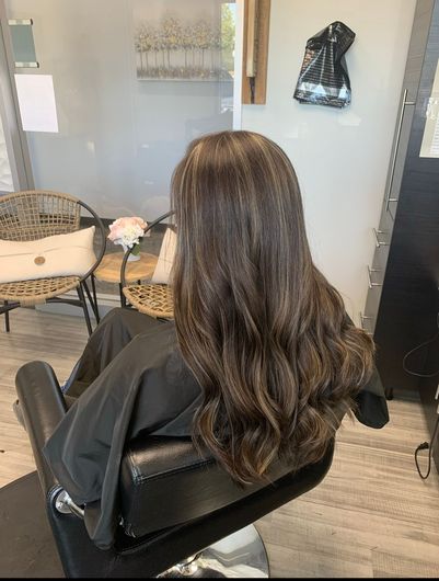 A woman with long brown hair is sitting in a chair in a salon.