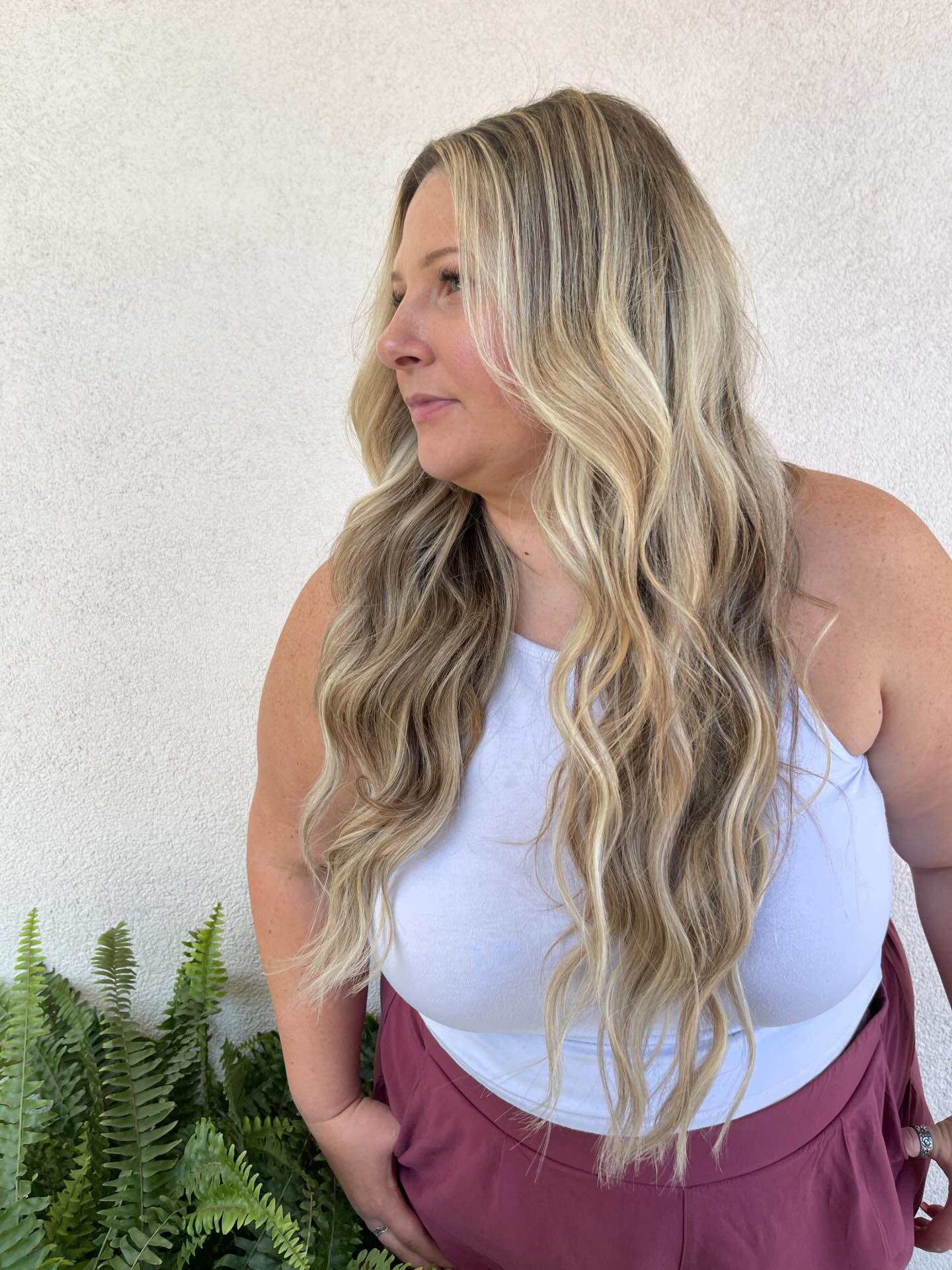 A woman with long blonde hair is wearing a white tank top and red shorts.