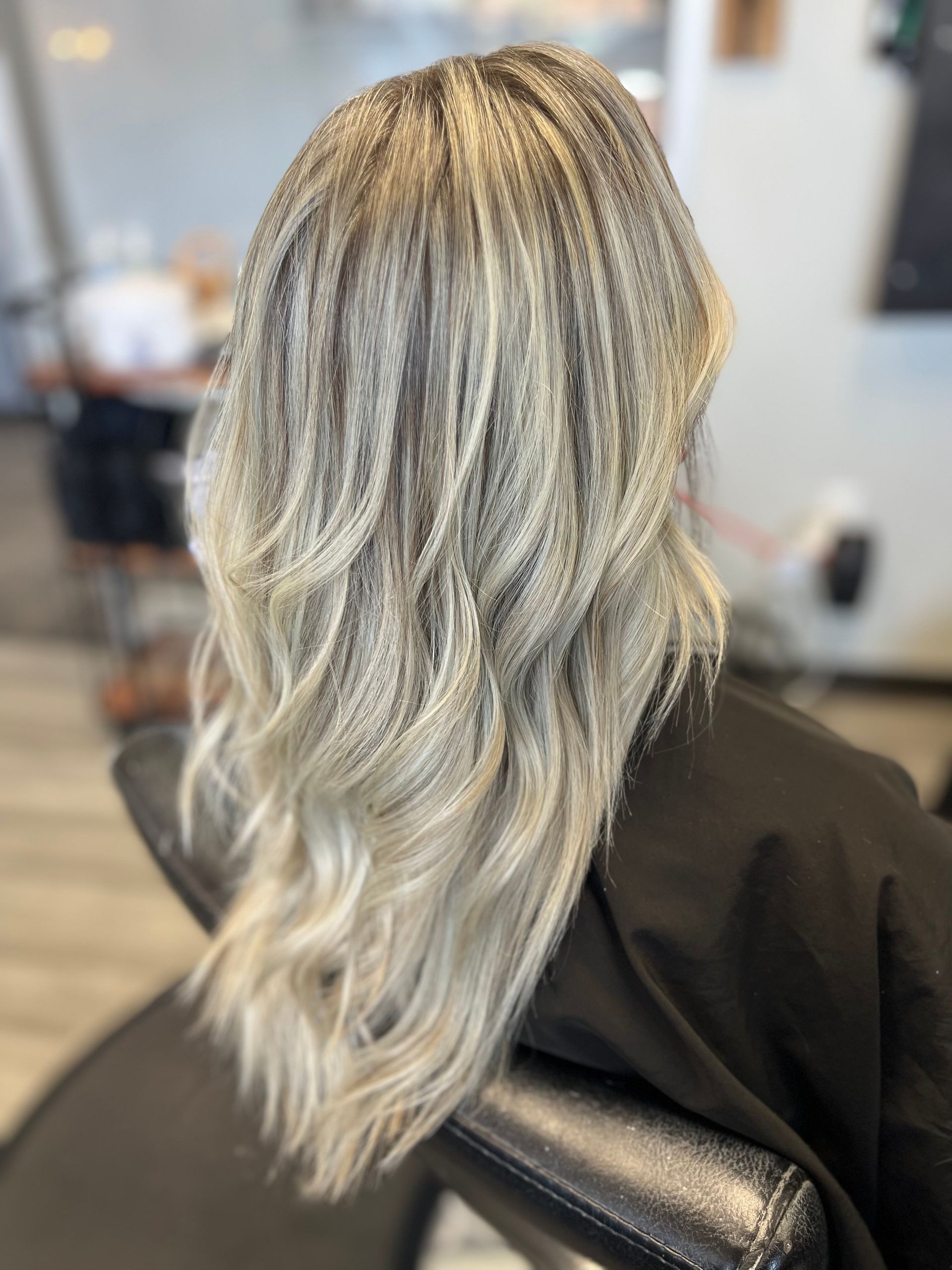 A woman with long blonde hair is sitting in a chair in a salon.
