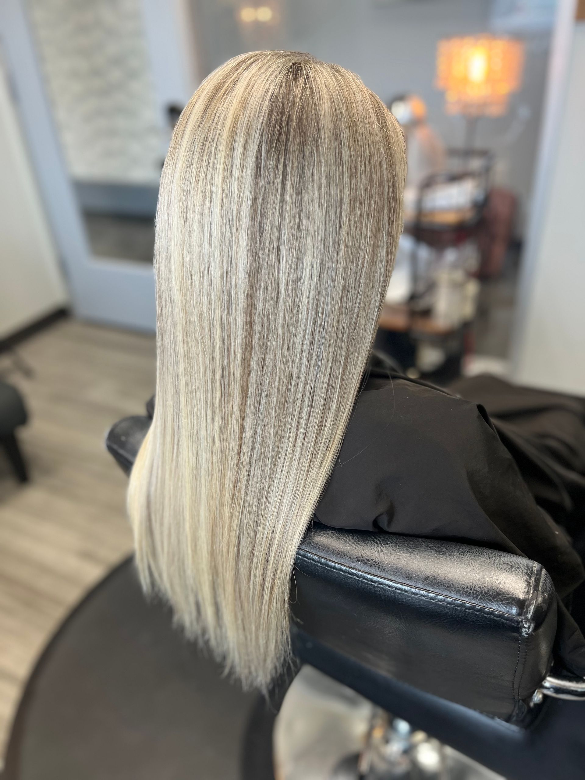 A woman with long blonde hair is sitting in a chair in a salon.