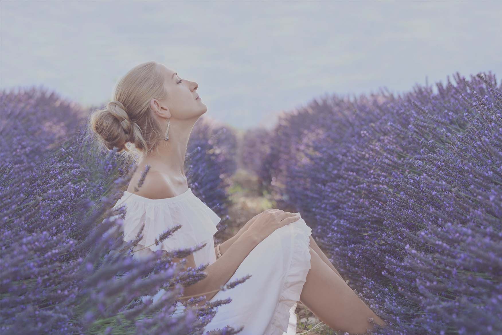 A woman in a white dress is sitting in a lavender field.