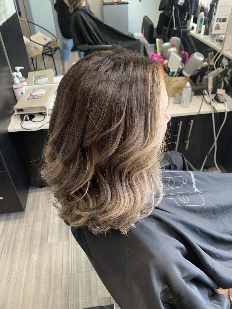 A woman is sitting in a chair at a hair salon getting her hair cut.