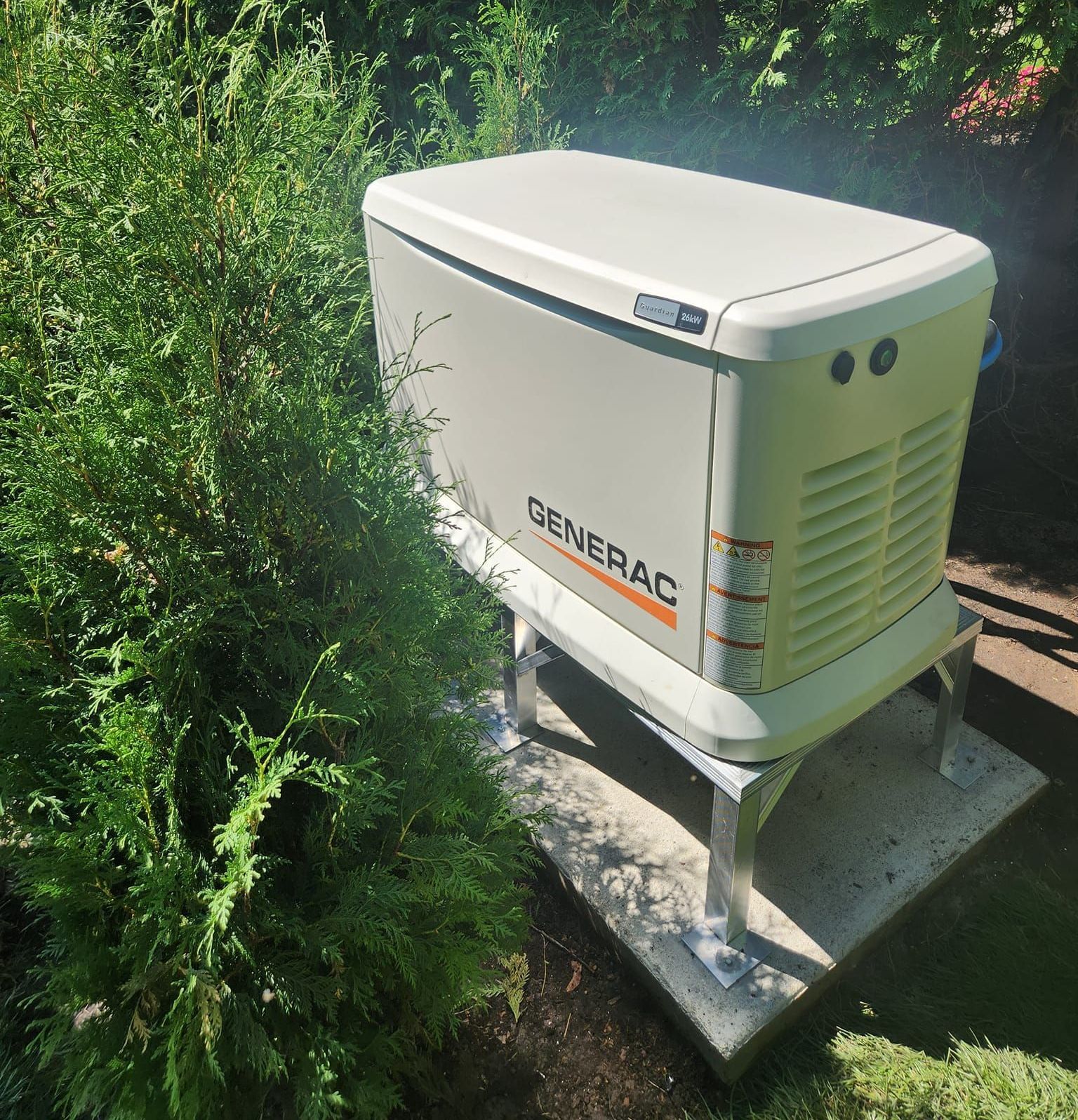 A generac generator is sitting on top of a concrete platform surrounded by trees.