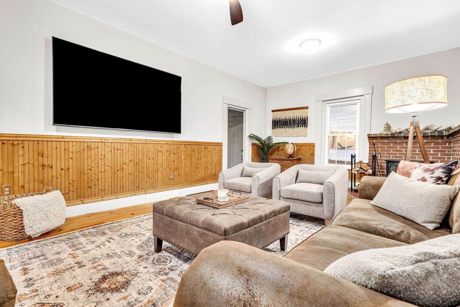 Cozy living room with a large TV, brown sofa, two armchairs, fireplace, and wooden accents.