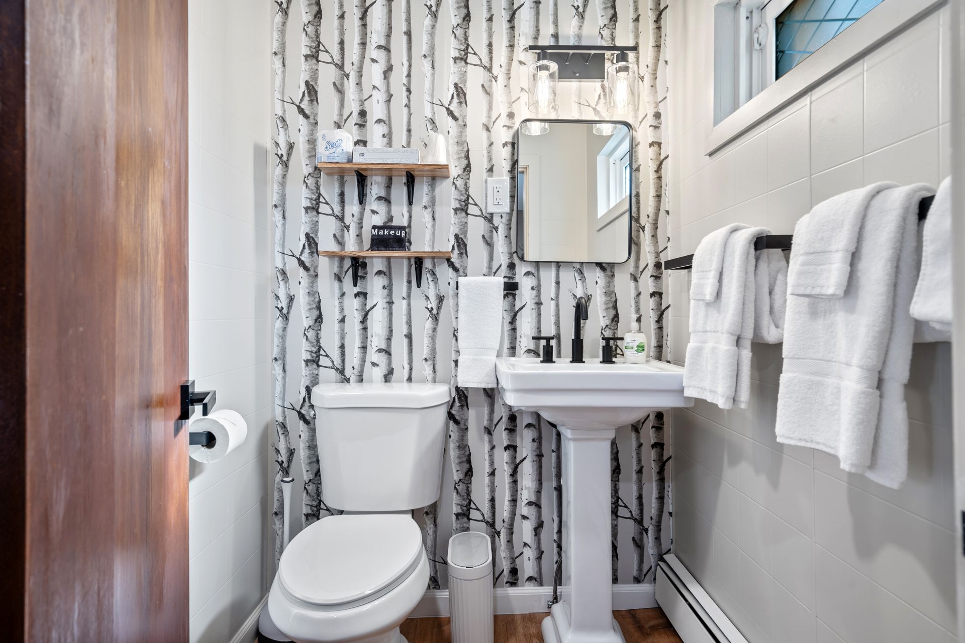Bathroom with birch tree wallpaper, a pedestal sink, and white towels.