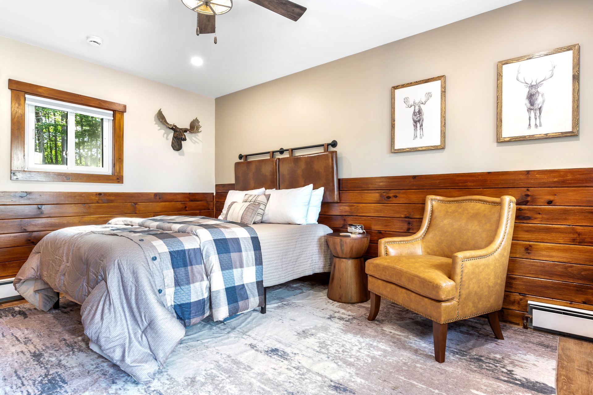Bedroom with wood accent wall, bed, armchair, artwork, and antler decor.