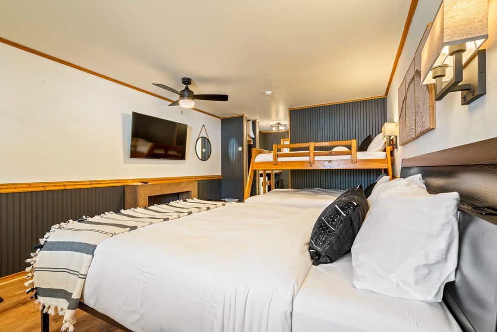 Hotel room with a queen bed, bunk beds, wood paneling, and a small table.