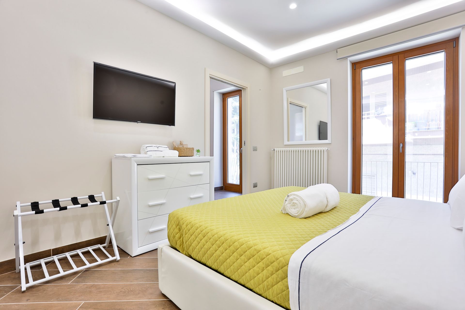 Camera d'albergo con letto, cassettiera, televisione e porte scorrevoli in vetro.