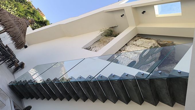 Un'area salotto esterna con patio, racchiusa da una struttura in legno con ampie vetrate, vista da dietro una recinzione metallica.