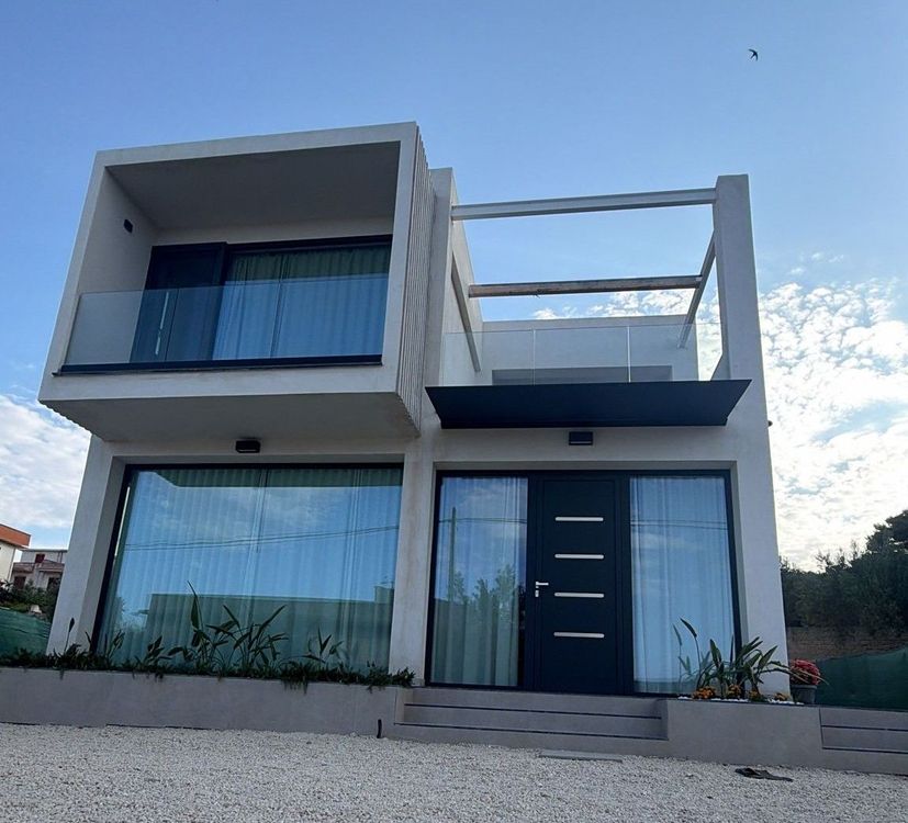 Un edificio moderno è caratterizzato da un'alta facciata continua in vetro che riflette il cielo, fiancheggiata da strutture bianche e condizionatori d'aria.