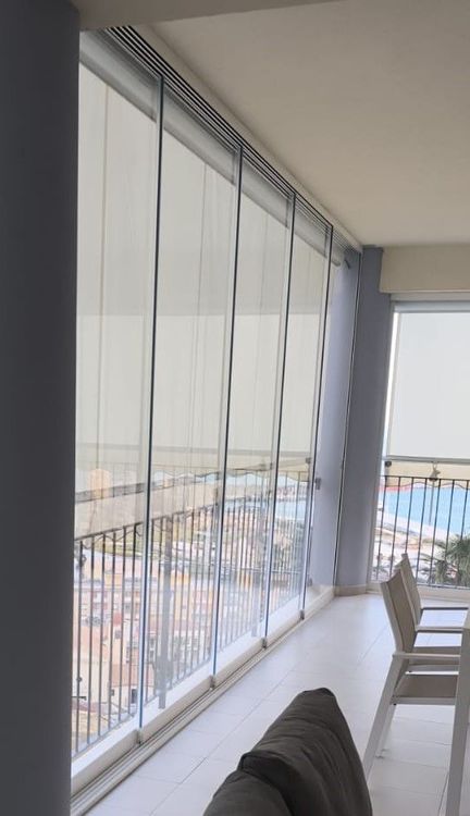Un edificio moderno è caratterizzato da un'alta facciata continua in vetro che riflette il cielo, fiancheggiata da strutture bianche e condizionatori d'aria.