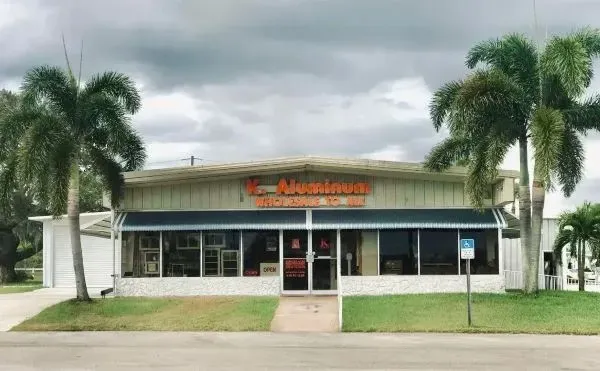 Small storefront with orange sign, palm trees, and cloudy sky in front.