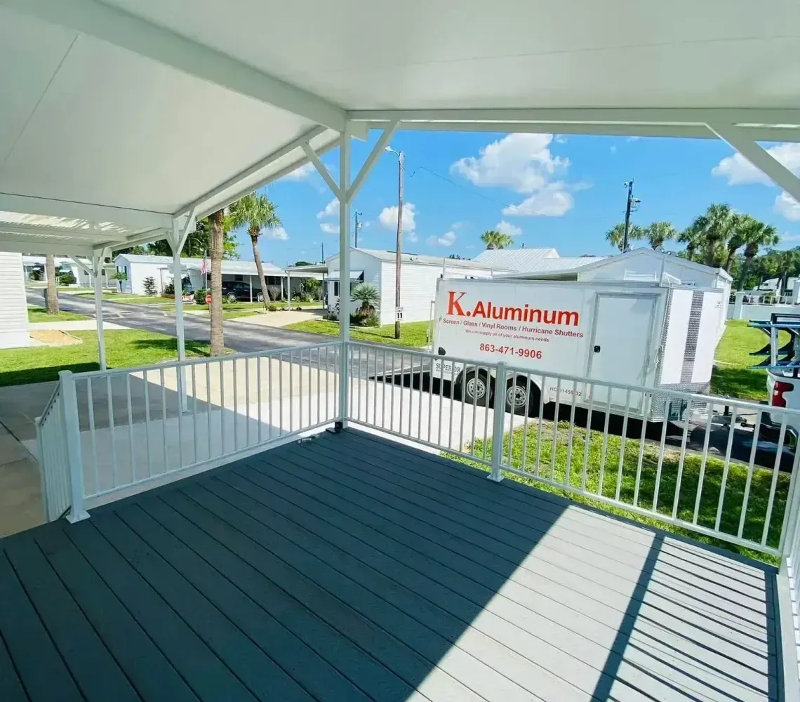 Covered porch with white railings, teal floor, and a view of parked trailers and blue sky.