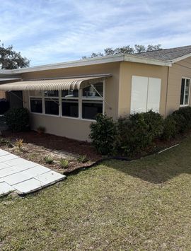 White two-story house with large windows, a striped awning, and palm shadows on the facade.