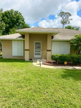 Single-story beige house with a front lawn, white shutters, and a small front porch under a blue sky