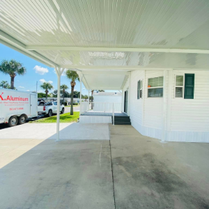 White house front porch with covered driveway, ramp, steps, and parked trucks on a sunny street
