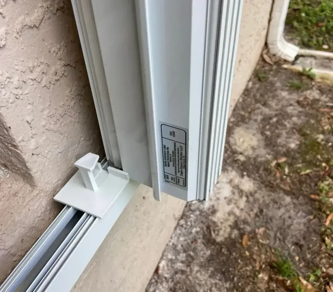 Close-up of a white sliding door track and frame beside a stucco wall and concrete ground.