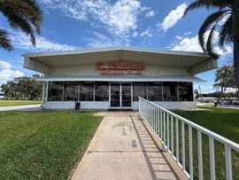 Small storefront with orange sign, palm trees, and cloudy sky in front.