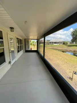 Covered porch with white railing and view of grassy yard and pond on a sunny day