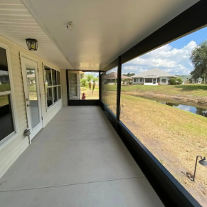 Covered porch with screened railing, white exterior doors, and a grassy yard with a pond view.