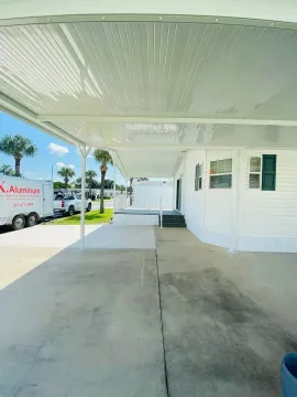 Covered driveway beside a white house, with concrete walkway, parked van, and bright sunny sky