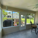 Screened porch with gray siding, sliding door, patio chair, and a view of a green backyard and neighboring houses